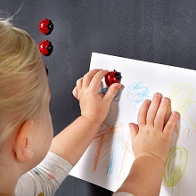 Ein kleines Mädchen hängt ihre Zeichnungen mit Glückskäfer-Magneten auf