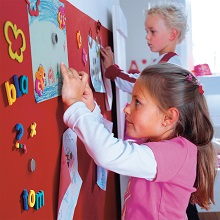 Zwei Kinder hängen ihre Zeichnungen mit Magneten an einer bunten Wand auf