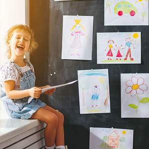 Ein kleines Mädchen freut sich, ihre bunten Kinderzeichnungen an der Magnetwand aufhängen zu können