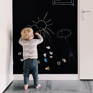Ein kleiner Junge malt begeistert eine Sonne an seine Wandtafelwand